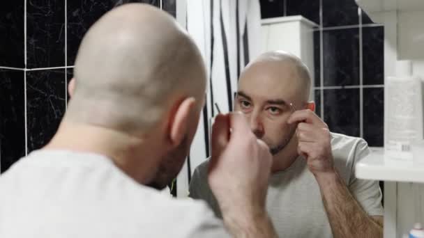 男人的家常便饭镜中的倒影 一个年轻英俊的白种人秃头男子用镊子拔眉毛的画像 皮肤护理 — 图库视频影像
