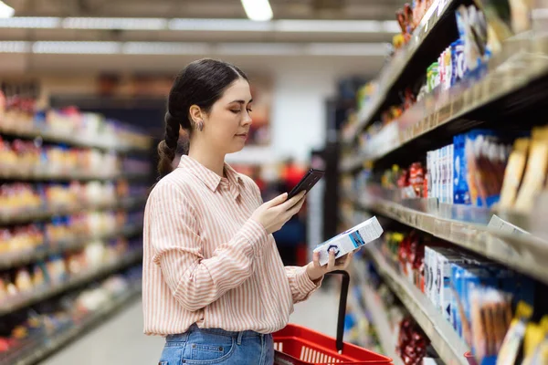 年轻白人妇女用智能手机扫描产品的Qr代码的侧视图 背景上有食物的贝壳 现代购物的概念 — 图库照片