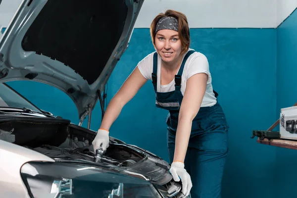 Smiling woman mechanic in gloves repairs car with wrench. The concept of women\'s equality.