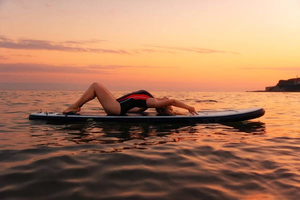 海の中のアップボードに横になってポーズをとるセクシーな若い女性 コピースペース 背景に沈む夕日 スポーツ 休暇の概念 — ストック写真