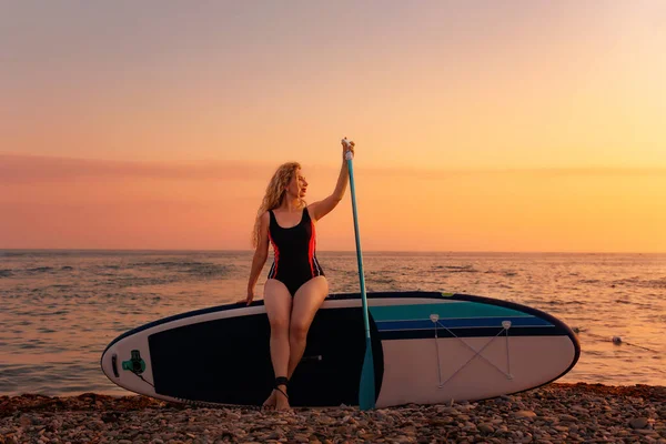 一个漂亮的年轻女子在日落和大海的背景下坐在木板上摆姿势 复制空间 海洋体育娱乐的概念 — 图库照片