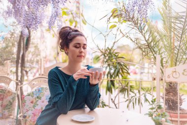 Rahatlama ve mutluluk. Yalnız, hoş, beyaz bir kadın, Wisteria çiçekli eski bir kafede bir fincan kahve içiyor. Psikoloji ve bencillik kavramı.