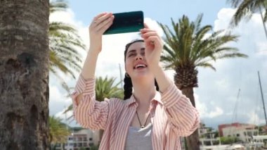 Genç ve mutlu bir kadının görüntüsü akıllı telefonu tutar ve video çeker. Arka planda avuç içi ve deniz kuvvetleri. Yaz tatili