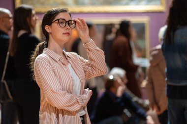 Sergiye bakan beyaz bir kadının portresi. Arka planda insanlar ve şaheserler var. Müze Günü Konsepti.