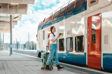 Beyaz bir kadın bavulunu tutuyor ve trenle yola çıkıyor. Seyahat, online rezervasyon ve tatil kavramı.