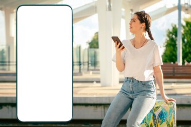 Güzel genç bir bayan bavulunun üzerinde oturuyor ve ayrılışını bekliyor, cep telefonu kullanıyor. Model yapıp uzayı kopyalayan büyük bir akıllı telefon. Modern seyahat ve tatil kavramı.