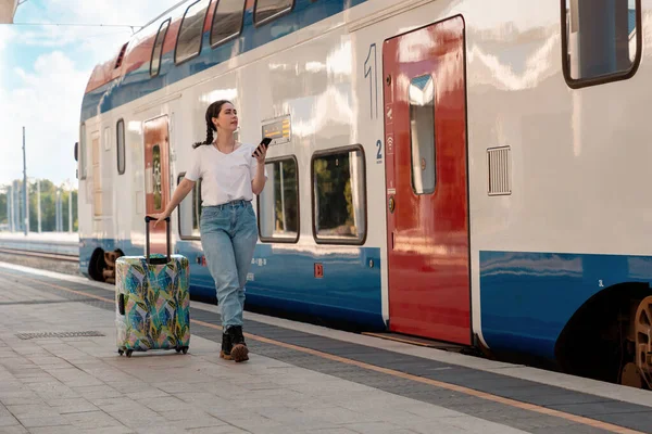 stock image Young pretty woman walking to departure holds her luggage. Train station is in background. Concept of vacation and business trip.