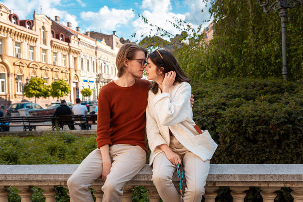 Young Caucasian couple relax in park sitting on ballustrade. Romantic date in Valentine's Day.