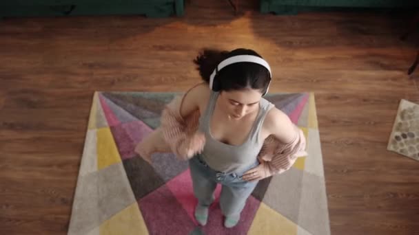 ヘッドフォン美しいダンスを着ている幸せな若い白人女性のトップビュー ホーム 週末パーティー — ストック動画