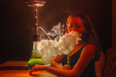 Seksi genç bir kadın nargile içiyor ve burun deliklerinden buhar salıyor. Kırmızı renk. Gece hayatı..