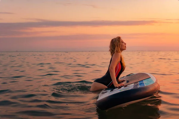 海の中のアップボードで水着姿のセクシーな若い女性 コピースペース 背景に沈む夕日 スポーツと休暇の概念 — ストック写真