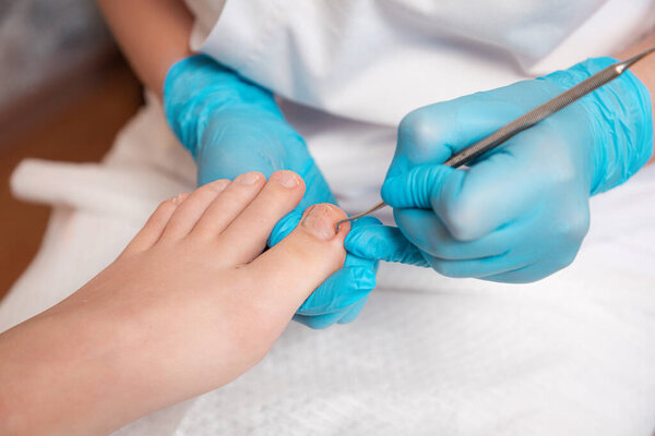 Chiropodist does a pedicure for the client's foot, cleaning the nails with a double-sided curette. Close up. The concept of salon professional nail care and podology.