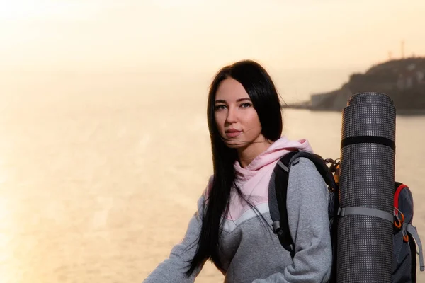 ハイキングとスポーツレクリエーションのコンセプト 美しい若い女性の肖像画 彼女の背後にある観光バックパック 日没と海に対して コピースペース — ストック写真