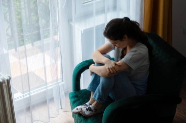 Yeşil kadife koltukta oturan, elleri dizlerinde katlanmış, üzgün, beyaz kadın manzarası. Depresyon, psikoloji ve akıl sağlığı sorunları kavramı.