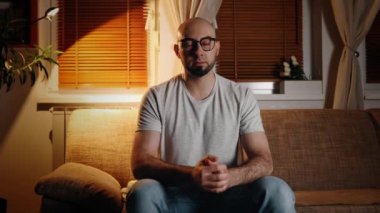 Web konferansı ve uzaktan çalışma. Gözlüklü, video konuşmasında konuşan beyaz sakallı yakışıklı bir adamın portresi. Akşam ışığı ve sıcak iç mekan. Serbest çalışma ve online röportaj kavramı.