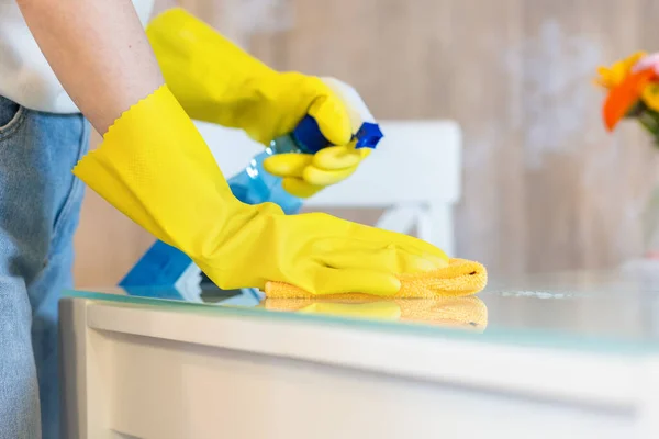 Woman in rubber gloves sprays cleanser and wipes table with rag. Close up. Cleaning service and chores.