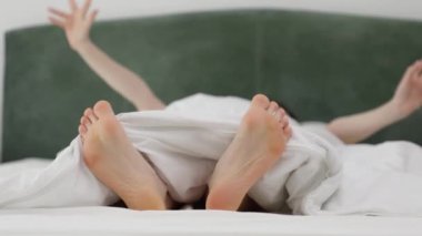 Beyaz yatakta tembelce uzanan bir kadın. Battaniyenin altından kadın bacakları görünüyor. Rahatlama ve tatil kavramı