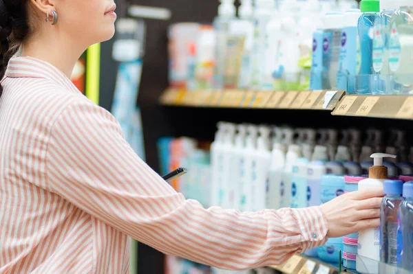 Close up of woman takes cosmetic bottle from shelf. Choice of care cosmetics in supermarket. Concept of shopping and purchase.