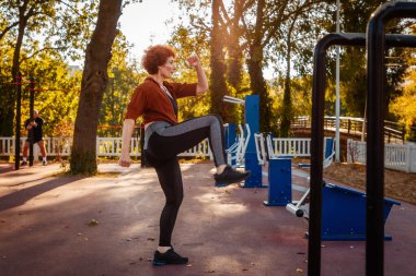 Orta yaşlı beyaz kadının mutlu gülüşünün yan görüntüsü aerobik yapıyor. Şehir parkındaki spor anlayışı.
