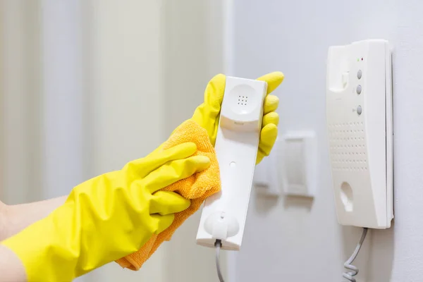 Housewife in yellow rubber gloves wipes telephone receiver. Hands close-up. Cleaning and household chores.