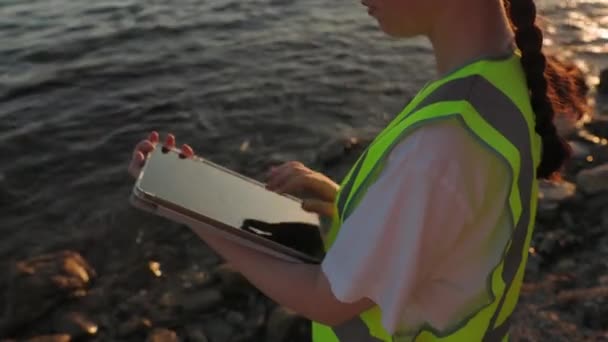 ベストを着てタブレットを使用するボランティアの閉鎖 背景にある海とビーチ 環境汚染 生態学研究のコンセプト — ストック動画