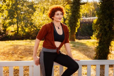 Beyaz ahşap çitlerde oturan gülümseyen güzel yetişkin kadın. Arka planda sonbahar ormanı. Sağlıklı yaşam tarzı kavramı