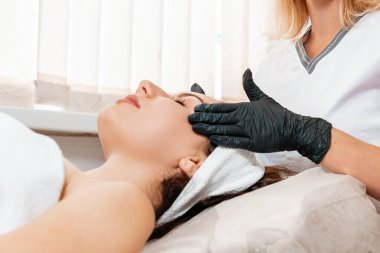 Kozmetoloji prosedürleri. Profesyonel güzellik uzmanı kuafördeki müşteriye yüz masajı yapıyor. Kadın yüzünü kapat. Gençleştirme ve kaldırma kavramı.