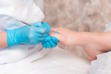 A chiropodist does a pedicure for the client's feet, cleaning the nails with a double-sided curette. Close up. The concept of salon professional nail care.