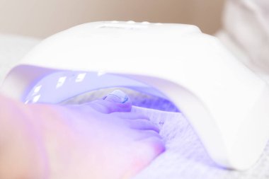 A woman's foot with a pedicure and titanium thread on the thumb lies under a UV lamp for drying varnish. Close-up. Podology and pedicure concept.