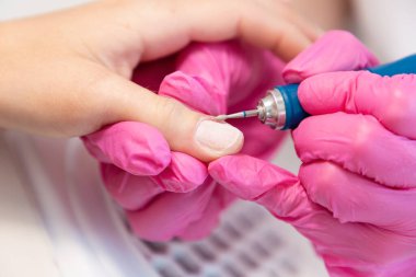 Pembe tıp eldivenli bir manikür ustası müşterinin tırnak derisini donanım dosyasıyla doldurmuş. Yakın plan. Manikür ve kuaför salonu profesyonel tırnak bakımı kavramı.