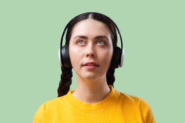 Teknik destek ve yardım hattı. Kulaklıklı, yeşil arka planda müzik dinleyen beyaz bir kadının portresi. Öğrenme ve podcast konsepti.