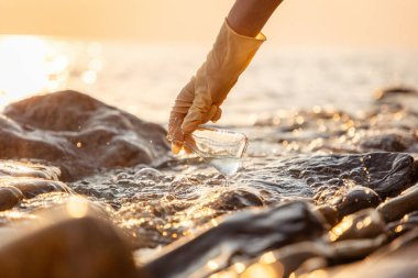 Eline kauçuk eldiven takıp okyanustan gelen su numunesini test et. Su kaynaklarını geri dönüştürme ve Dünya 'yı kurtarma kavramı.