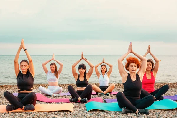 Group of Caucasian women wearing sportswear does yoga on beach. Copy space. Concept of meditation and wellness.