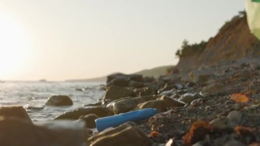 Kadın gönüllü şişeyi alıp vahşi çakıl taşlı sahilde çöp torbasına koyuyor. Çevre kirliliği kavramı