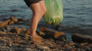 Gönüllü bir kadının plastik çöp torbası taşıdığını ve vahşi çakıl taşlı sahillerde yürüdüğünü yakından görmek plastik şişeleri kaldırıyor. Çevre kirliliği kavramı ve gezegeni kurtarmak