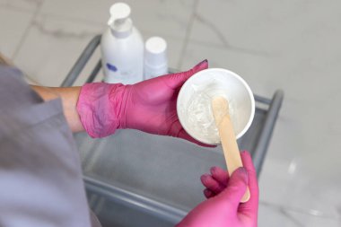 Lazer tüyü çıkarmak için jöleli spatulayla karıştırılmış ellerin üst görüntüsünü kapat. Kozmetik ve cilt bakımı.