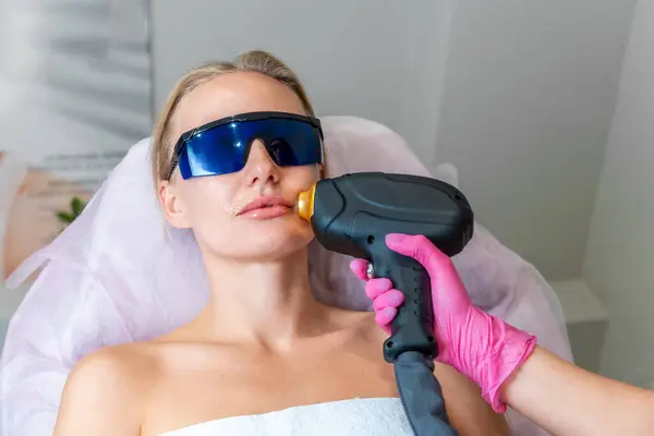 Portrait of young woman at laser hair removal session. Beautician removes hair above client\'s upper lip. Concept of laser hair removal and aesthetic medicine.