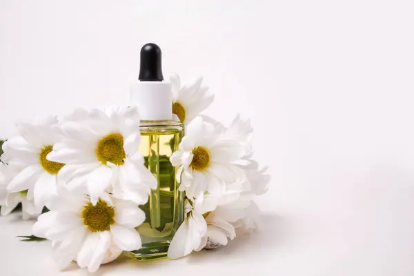 Close up of a glass bottle with cosmetic decorated with chamomile flowers. White background with copy space. The concept of organic natural cosmetics.