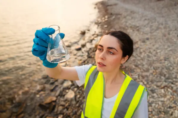 Top view of young Caucasian woman wearing protective gloves research water test. Ecologist examines chemical sample flask. Concept of pollution water and ecology.