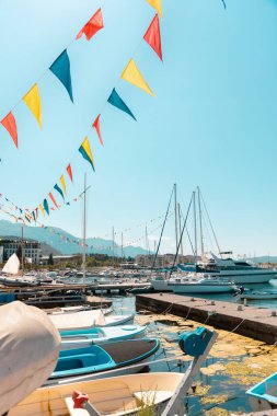 Akdeniz kıyısında tekneleri ve bayrakları olan güzel güneşli bir köy iskelesi manzarası. Tatil köyünde yaz tatili. Dikey yönelim.