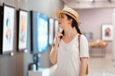 Tarihsel eğitim. Hasır şapka giyen genç beyaz kadın galeride tablolara hayran. Müze ve kültür eğitimi kavramı.