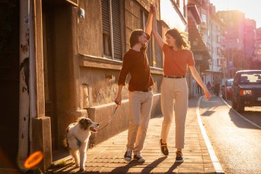 Sokakta dans eden bir çiftin romantik randevusu. Bir adam ve bir kadın köpek evcil hayvanıyla yürüyor. Arkaplanda gün batımı ışığı.