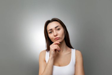 Fikir ve bilgi arama kavramı. Eli çenesinde olan genç, düşünceli, beyaz bir kadının portresi. Gri arkaplan ve ışık. Boşluğu kopyala.