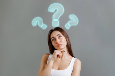 Fikir ve bilgi arama kavramı. Soru işaretlerine bakan düşünceli beyaz bir kadının portresi. Gri arka plan. Boşluğu kopyala.