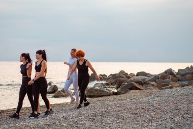 Koşudan sonra kumsalda sıra sıra yürüyen bir grup beyaz kadın. Arka planda deniz ve ufukta. Uzayı kopyala Sağlıklı yaşam tarzı ve refah kavramı.