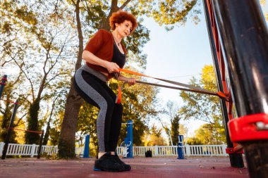 Yetişkin, güçlü, beyaz kadın spor alanında elastik bant ile esneme hareketleri yapıyor..