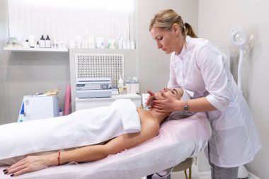 Profesyonel kozmetik uzmanı kadınlar için yüz gençleştirme masajı yapıyor. Yaşlanma önleme prosedürleri ve kozmetoloji.