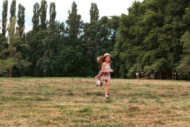 Yaz okulu tatili. Hasır şapkalı ve elbiseli mutlu küçük kız parkta koşuyor. Uzayı kopyala Çocukluk ve Çocuk Günü kavramı.