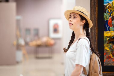 Tarihsel eğitim. Galeride resimlere hayran olan, hasır şapka takan güzel beyaz kadın öğrencinin portresi. Uzayı kopyala Müze ve kültür eğitimi kavramı.