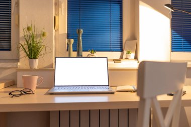 Beyaz ekranlı bir dizüstü bilgisayar ve merkez ofisteki masanın üstünde bir maket. Uzaktan çalışma, çevrimiçi eğitim ve serbest çalışma kavramı.